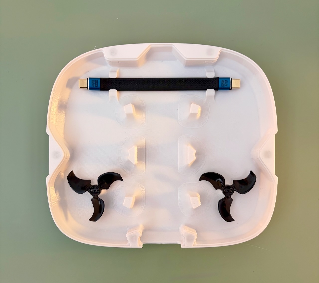 White bottom half of the DJI Neo 2 case holding two spare propellers and a USB-C cable